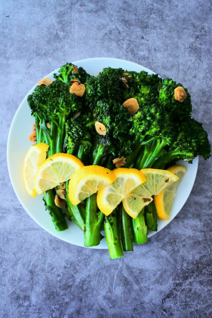 An overhead image of pan-sauteed broccolini with garlic on a plate with lemon wedges.