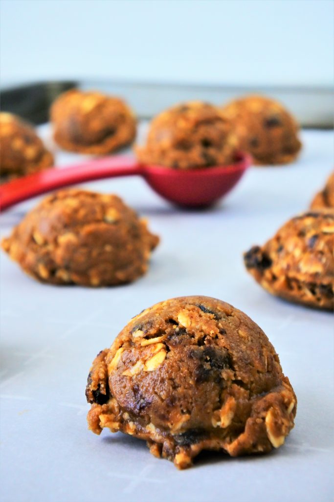 A close up image of oatmeal raisin cookie dough scooped onto parchment