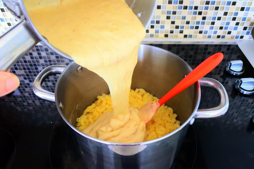 A close up image of pot of cooked gluten-free elbow pasta with a rich homemade cheese sauce being added to it.