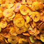 A close up image of freshly fried plantain chips dusted with salt on a plate