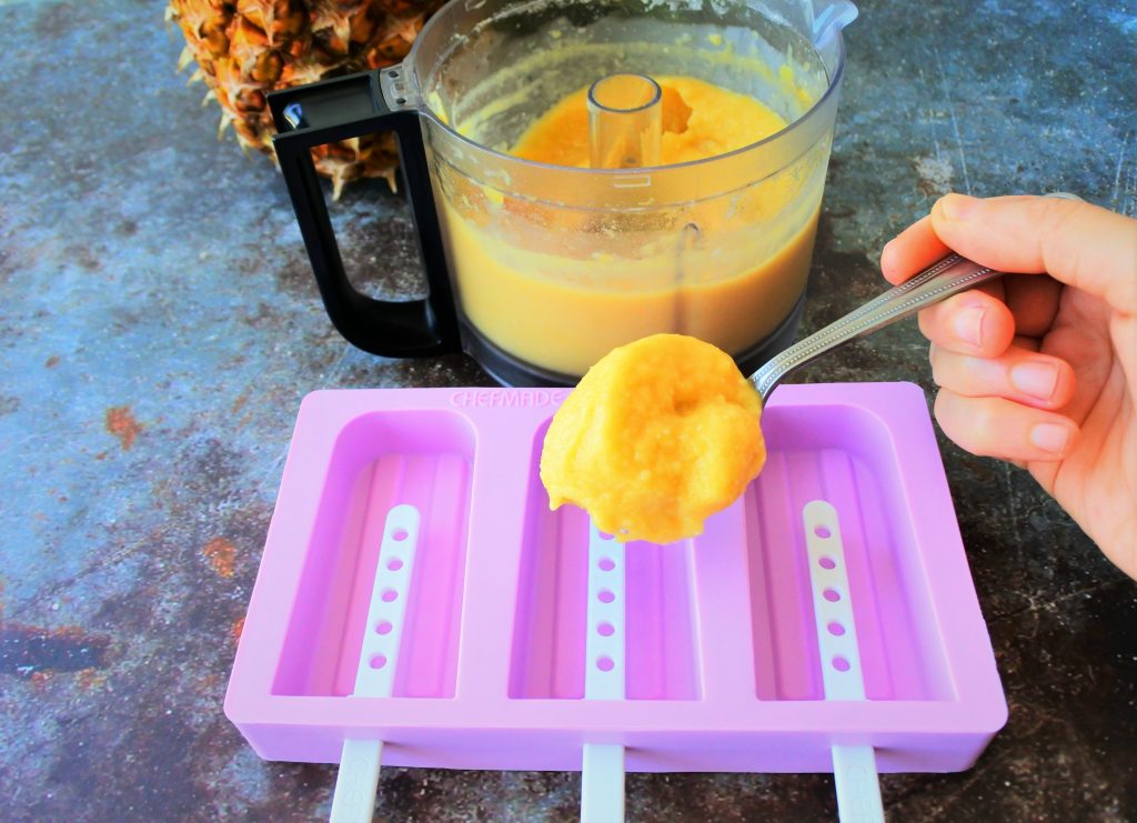 An angled image of a semi-frozen pureed pineapple mixture being spooned into a popsicle mold.