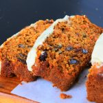 An angled image of slices of frosted carrot cake loaf on a wooden board