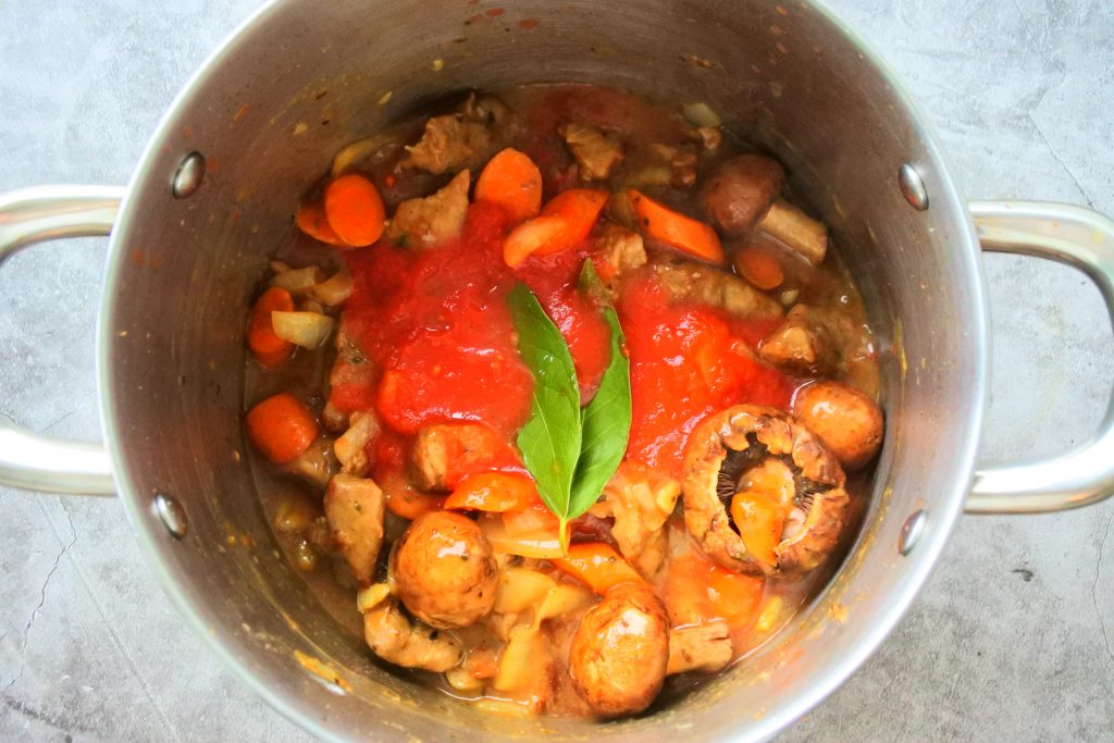An overhead image of a pot of spezzatino - veal and vegetable stew with the stock, tomato sauce, herbs and mushrooms