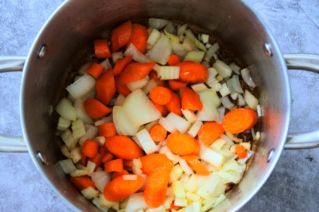 An overhead image of onion, carrots and celery (mirepoix) being added to a pot to sweat down and sauté.
