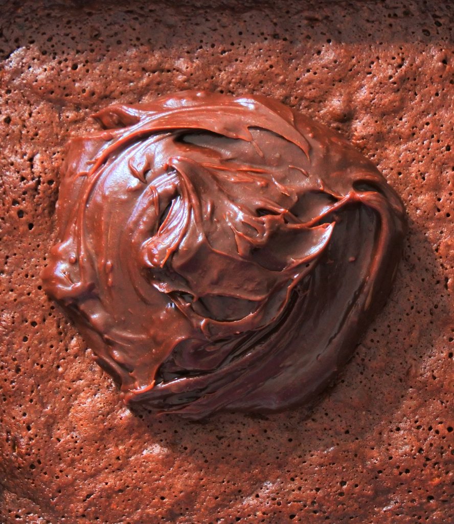An overhead close up image of chocolate ganache frosting on top of a pan of freshly baked and cooled brownies.