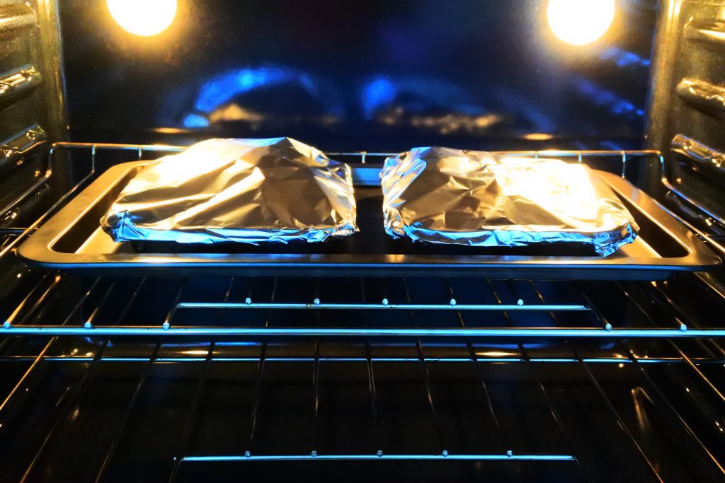 A head on image of a baking tray in the oven with foil tented muffin tins with potato au gratin