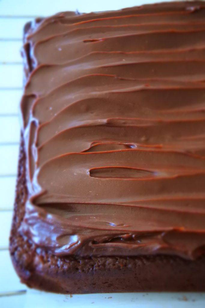 A close up image of chocolate ganache spread over fresh baked and cooled brownies