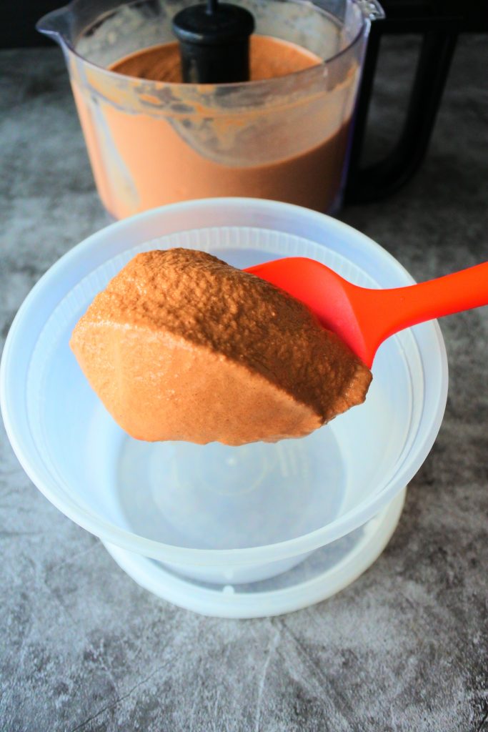 A close up angled image of frozen and blended ice cream base being scooped out a food processor and into a container.