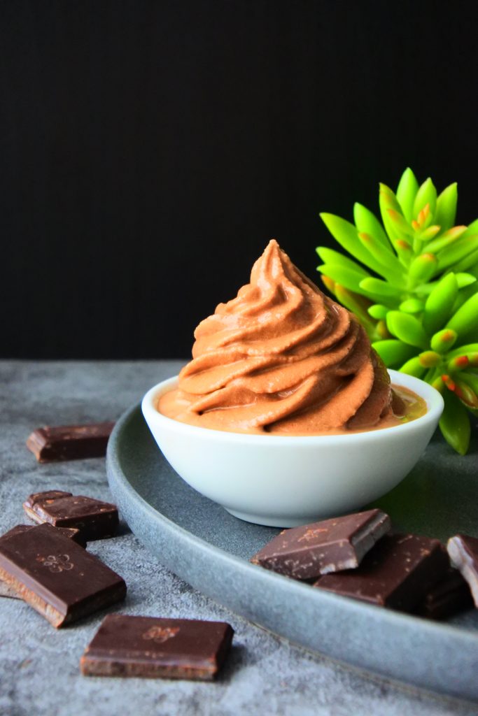 A piped swirl of soft serve textured ice cream surrounded by chunks of chocolate.