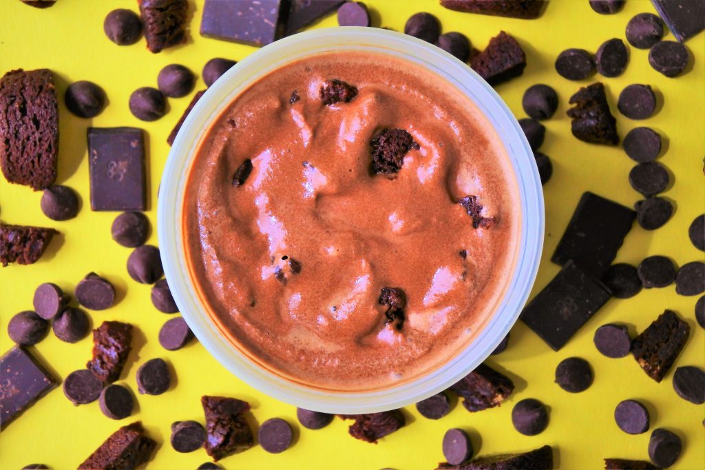 An overhead image of a container of semi-frozen ice cream base with chunks of brownie folded in