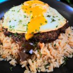 A close up image of a plate of moco loco with the egg yolk cut and running into the gravy