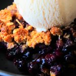 A close up image of a dish of blueberry crisp with a scoop of homemade vanilla ice cream