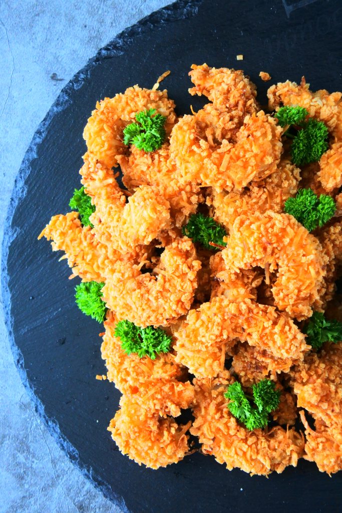 An overhead image of golden fried coconut shrimp on a slate plate