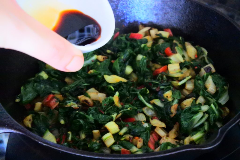 A close up image of soy sauce being added to sautéed swiss chard ohitashi