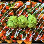 An overhead image of a tray cheesy beef nachos topped with salsa, sour cream, and guacamole