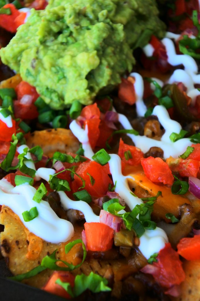 An angled image of cheesy beef nachos topped with sour cream, salsa and guacamole