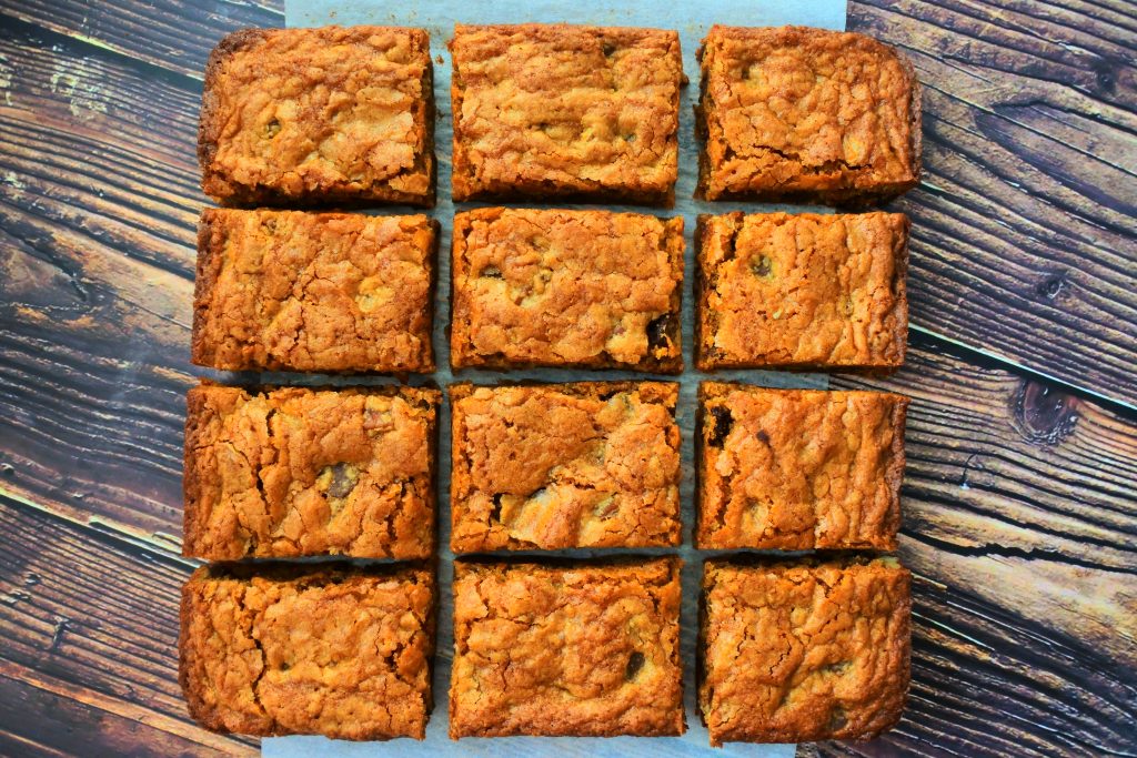 An overhead image of cut chocolate chip pecan blondies on parchment on a wooden surface
