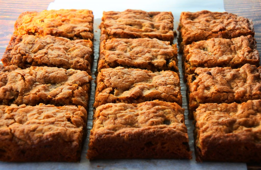 An angled image of cut chocolate chip pecan blondies on parchment on a wooden surface