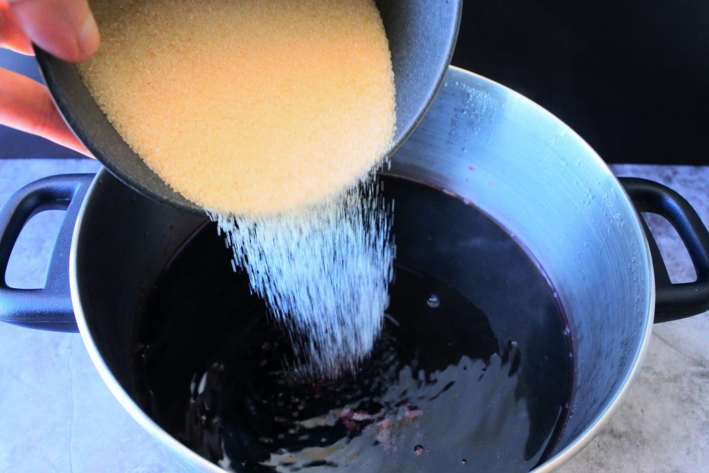 An overhead image showing a bowl of sugar being poured into freshly steeped sorrel drink.