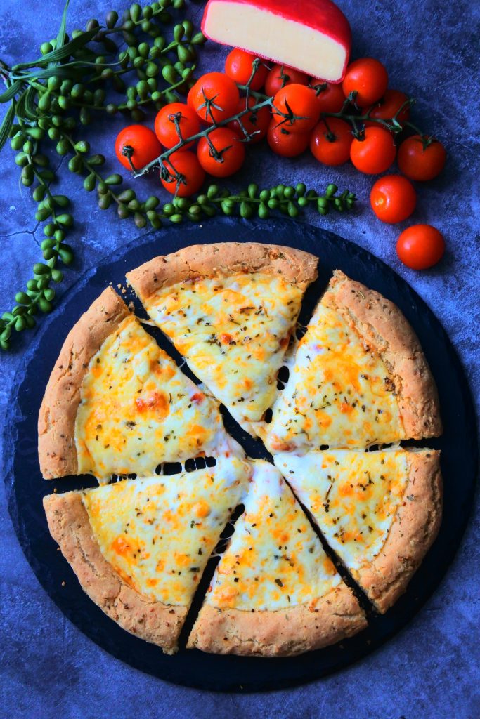 An overhead image of a sliced freshly baked cheesy pizza on a slate serving plate