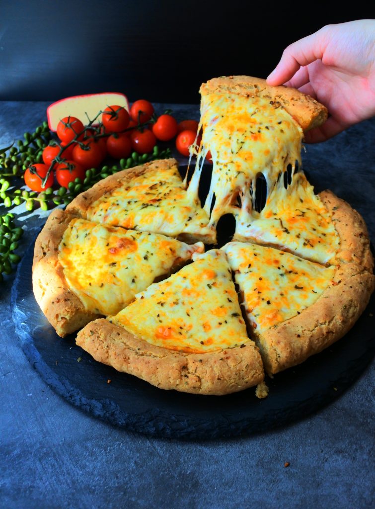 An angled image of a slice of freshly baked cheesy pizza on a slate serving plate with a hand lifting up a slice