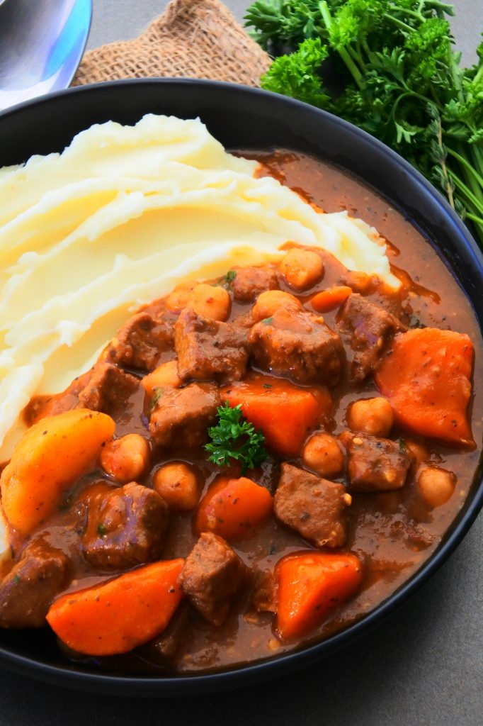 An angled image of a plate of classic beef stew and mashed potatoes