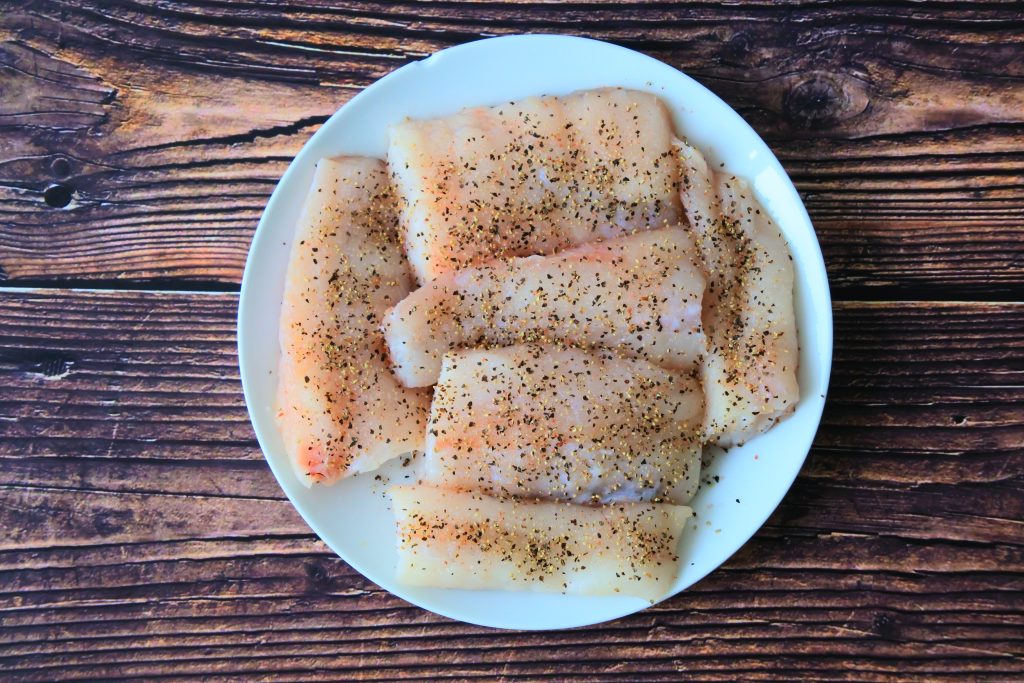 An overhead image of monkfish fillets seasoned with salt and pepper on a plate