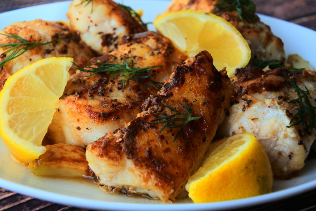 A head on image of a plate of pan-fried monkfish fillets with lemon wedges and fresh dill