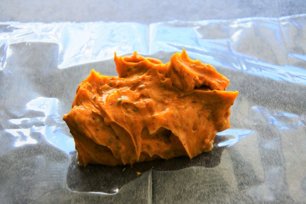 A head on image of softened, just mixed saffron compound butter scraped onto a sheet of plastic to be shaped and chilled for use.