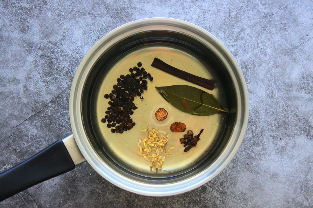 An overhead view of a small saucepan of aromatics and spices in oil
