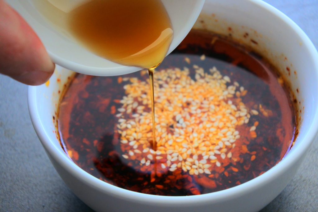 An overhead image of sesame oil being streamed into a bowl of steeped Chinese hot oil