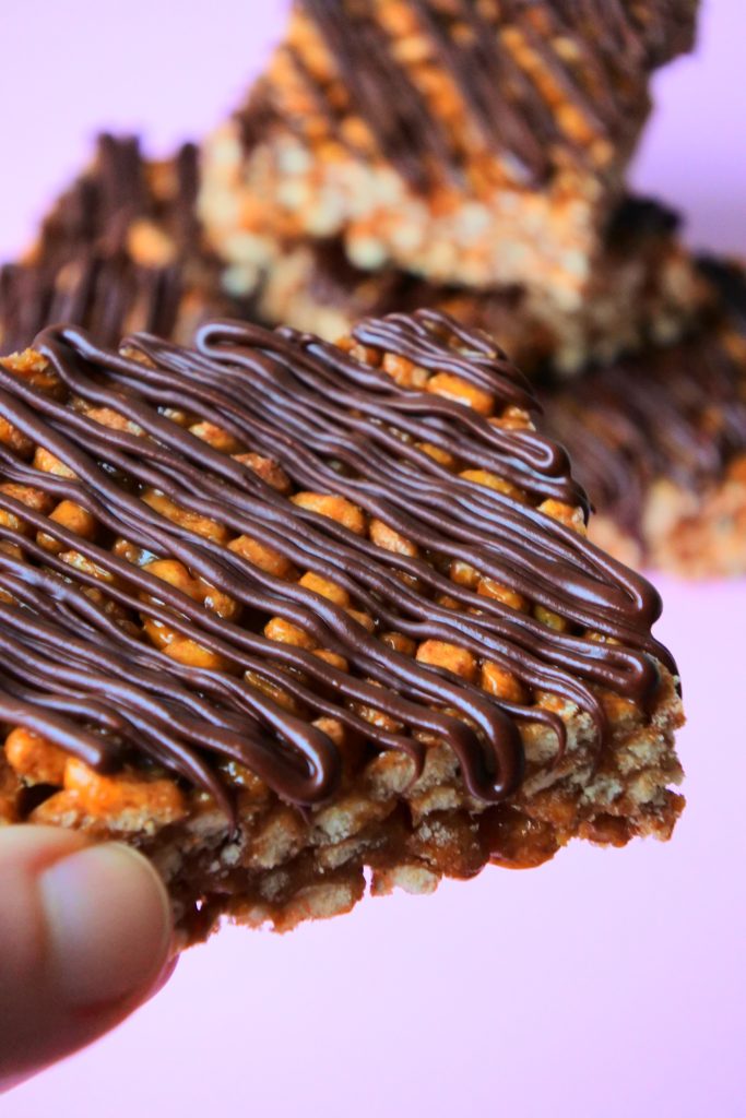 An angled image of a chocolate striped peanut butter rice crispy bar being held up close to the camera