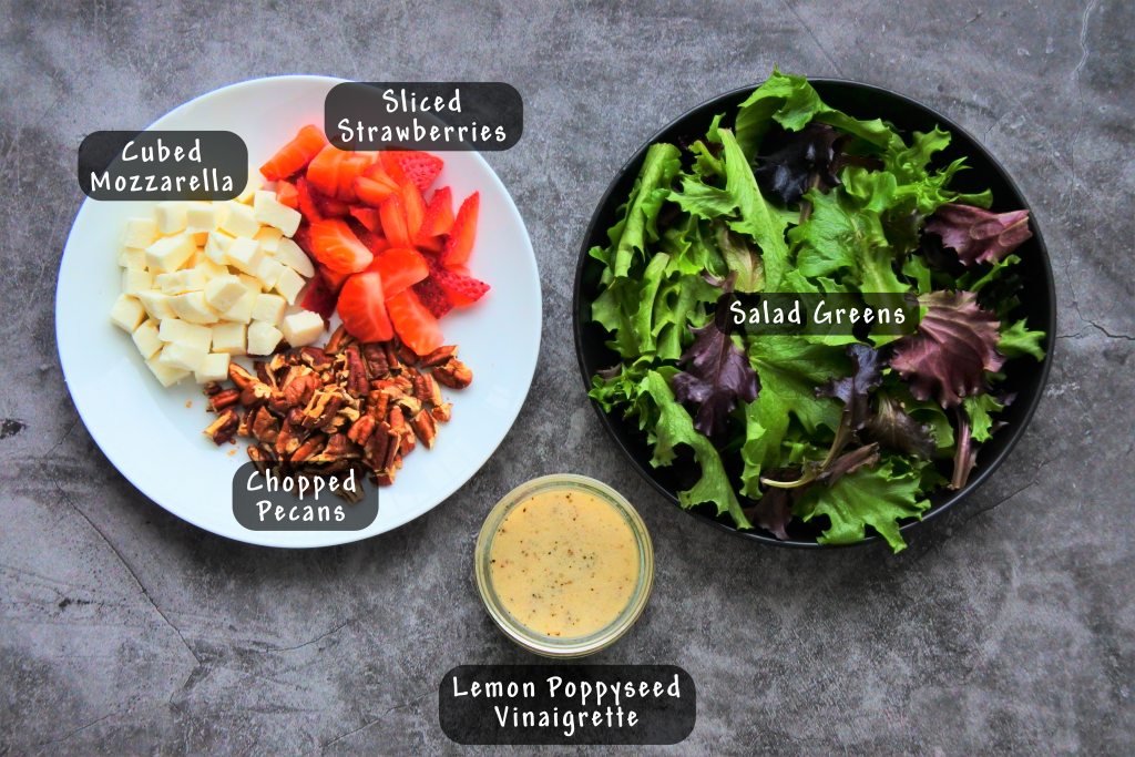 An overhead image of ingredients for a strawberry salad with a lemon poppy seed vinaigrette