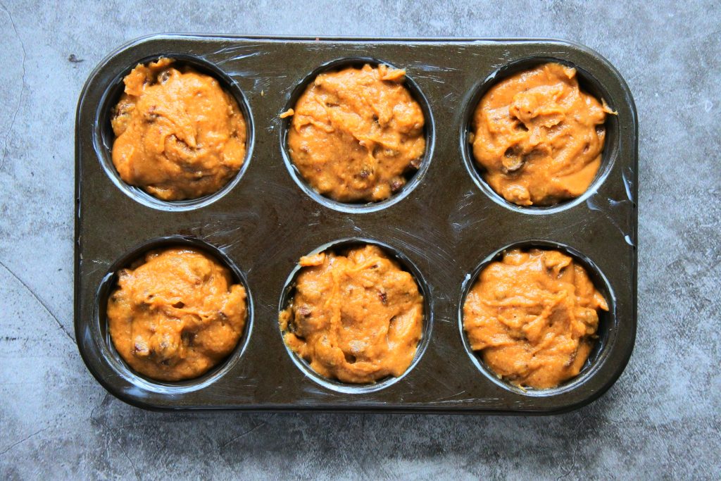 An overhead image of a greased muffin tin filled with the batter for a chocolate chip coffee muffins