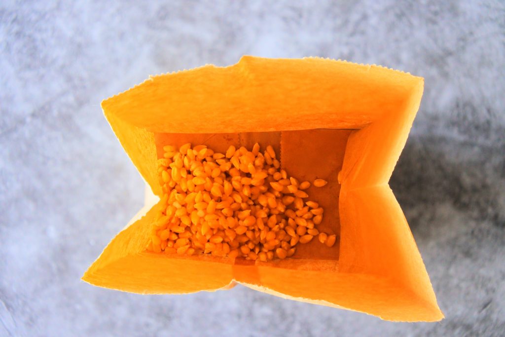 An overhead image of coconut oil rubbed popcorn kernels in a brown paper bag