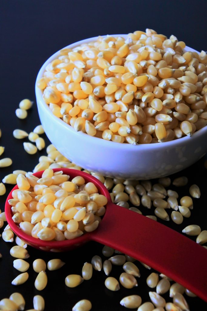 An angled image of kernels of white popcorn in a bowl with some in a red tablespoon measure