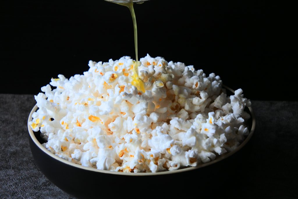 A head on image of butter being streamed over freshly popped popcorn in a bowl