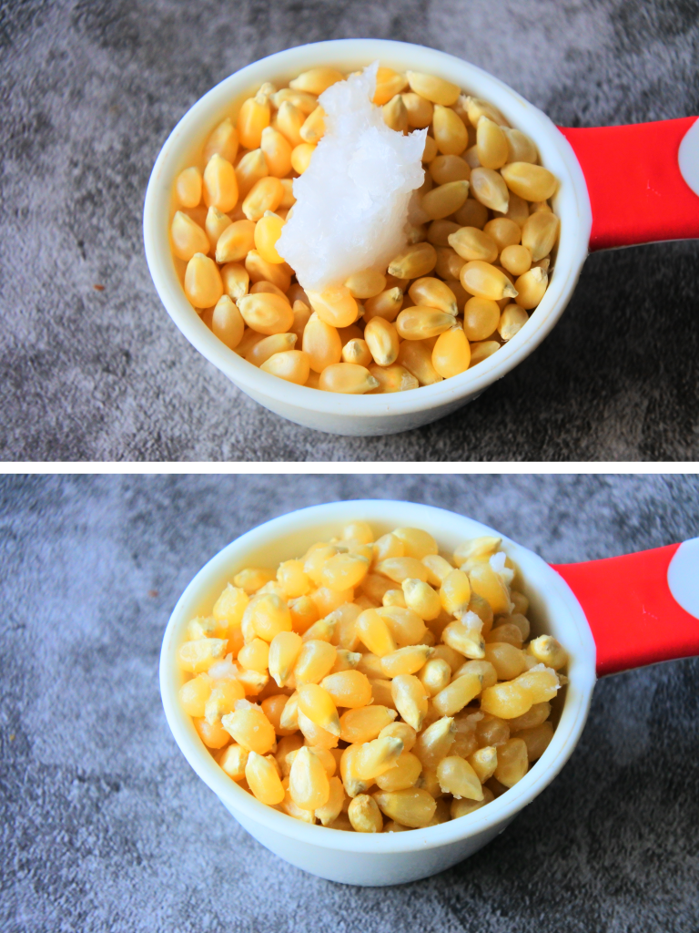 An angled overhead image of a scoop of unpopped popcorn kernels with a bit of coconut oil being rubbed onto the kernels