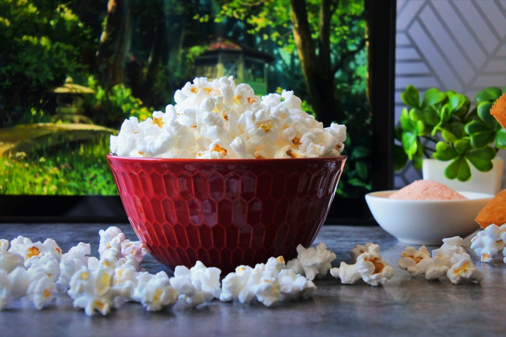 A head on image of popped popcorn in a red bowl on a counter top.