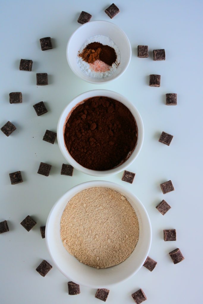 An overhead image of bowls of ingredients for a hot cocoa mix surrounded by chunks of chocolate