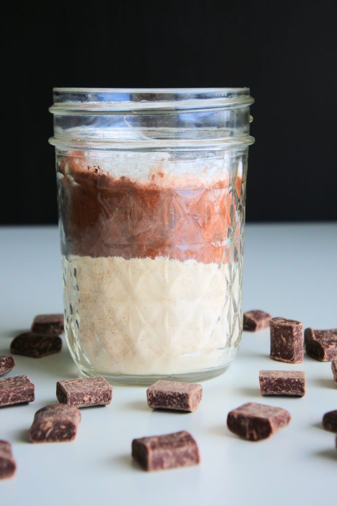 A head on image of the layers of ingredients for a hot cocoa mix in a jar surrounded by dark chocolate chunks