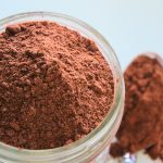A close up overhead image of a jar of hot cocoa mix with an out of focus spoon of hot cocoa mix below it