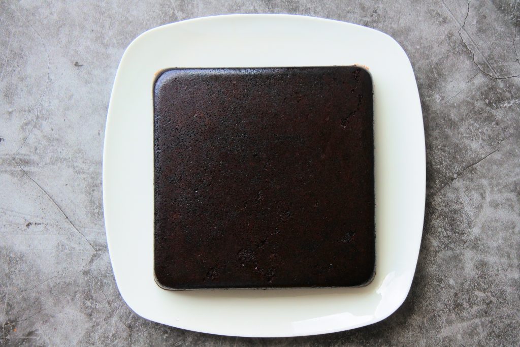 An overhead image of a baked Healthier Chocolate Cake that's been turned out onto a square plate with the underside now on top.