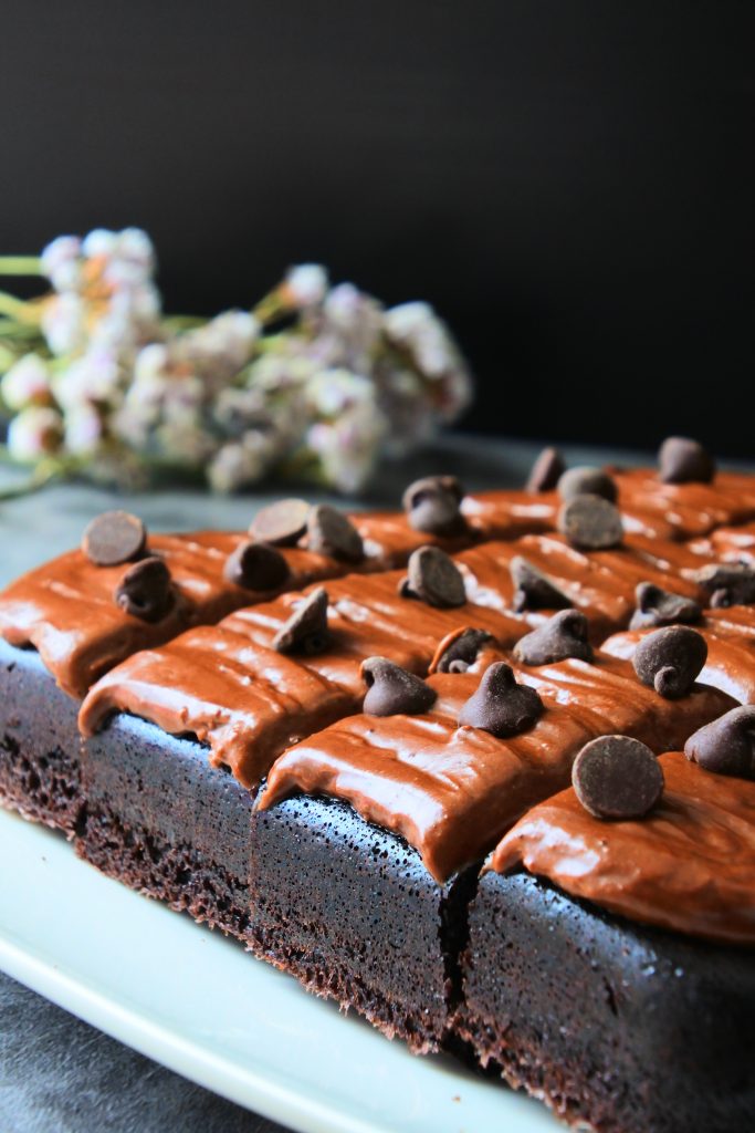 An angled image of Kitrusy's healthier chocolate cake frosted with chocolate frosting and topped with dark chocolate chips.