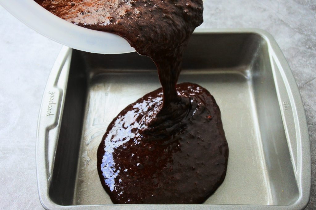 A head on angled image of batter for Kitrusy's healthier chocolate cake being poured into a greased 8x8 pan