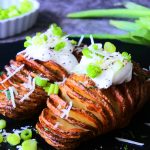 An angled image of crispy air-fried Hasselback potatoes topped with Greek yogurt, black pepper, spring onions and a sprinkle of Parmesan cheese