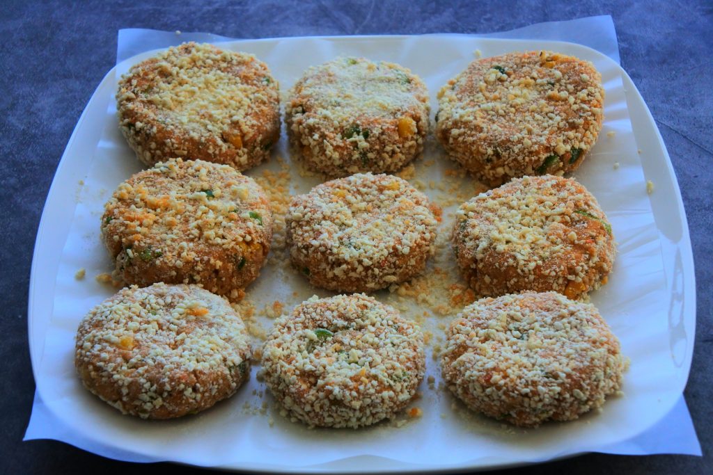 An angled image showing nine (gluten-free) panko-coated salmon patties on a sheet of parchment on top of a white plate.