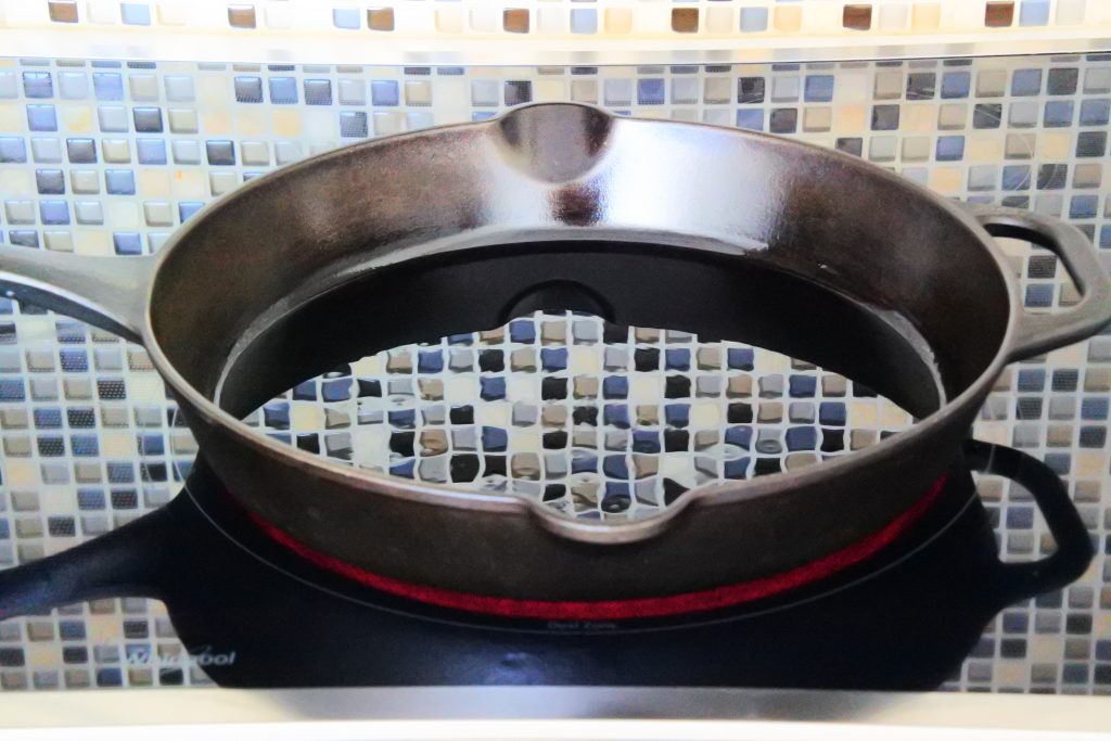 An angled head on image showing a cast iron skillet with enough oil to coat the bottom being heated to med-high heat.