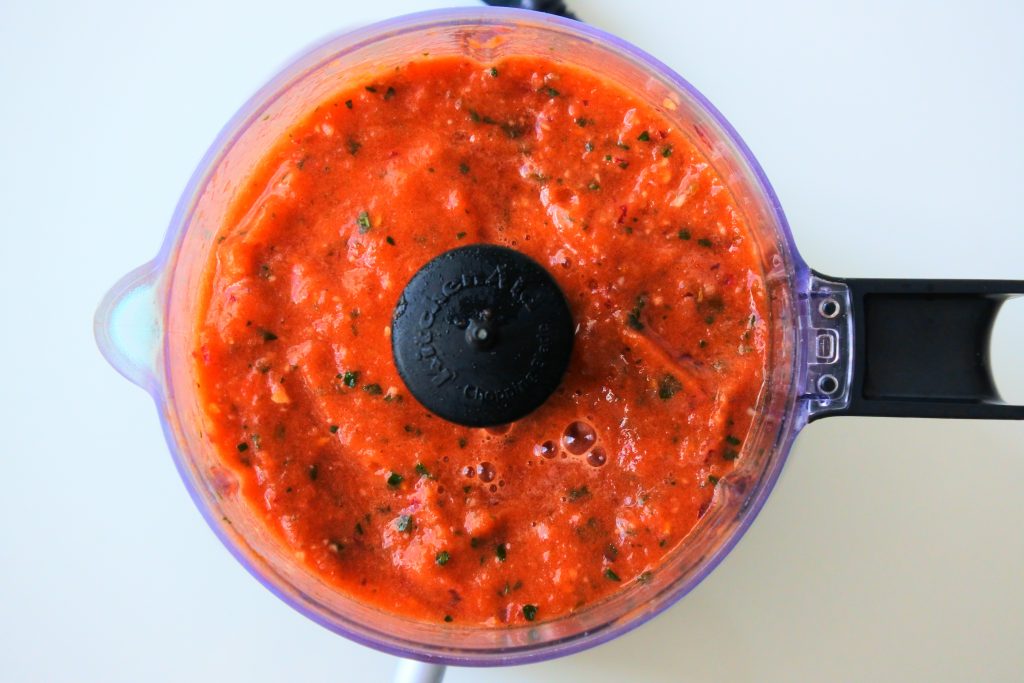 An overhead image of a mini food processor with blended tomato salsa