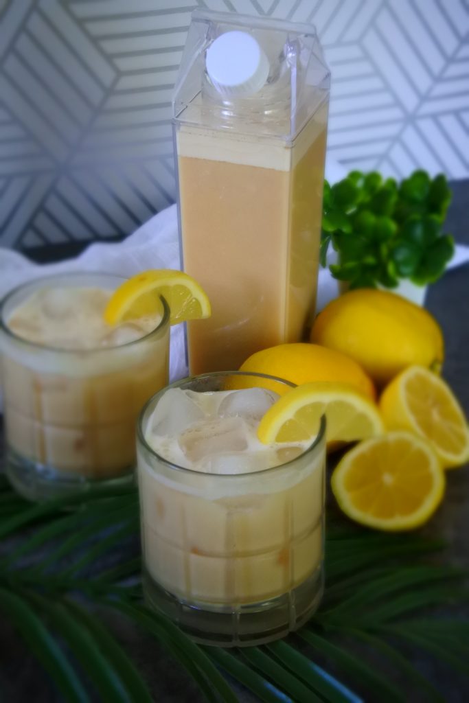 A close up angled image of a glass of Kitrusy's Creamy Dreamy Lemonade served over ice with a lemon wedge on the rim.
